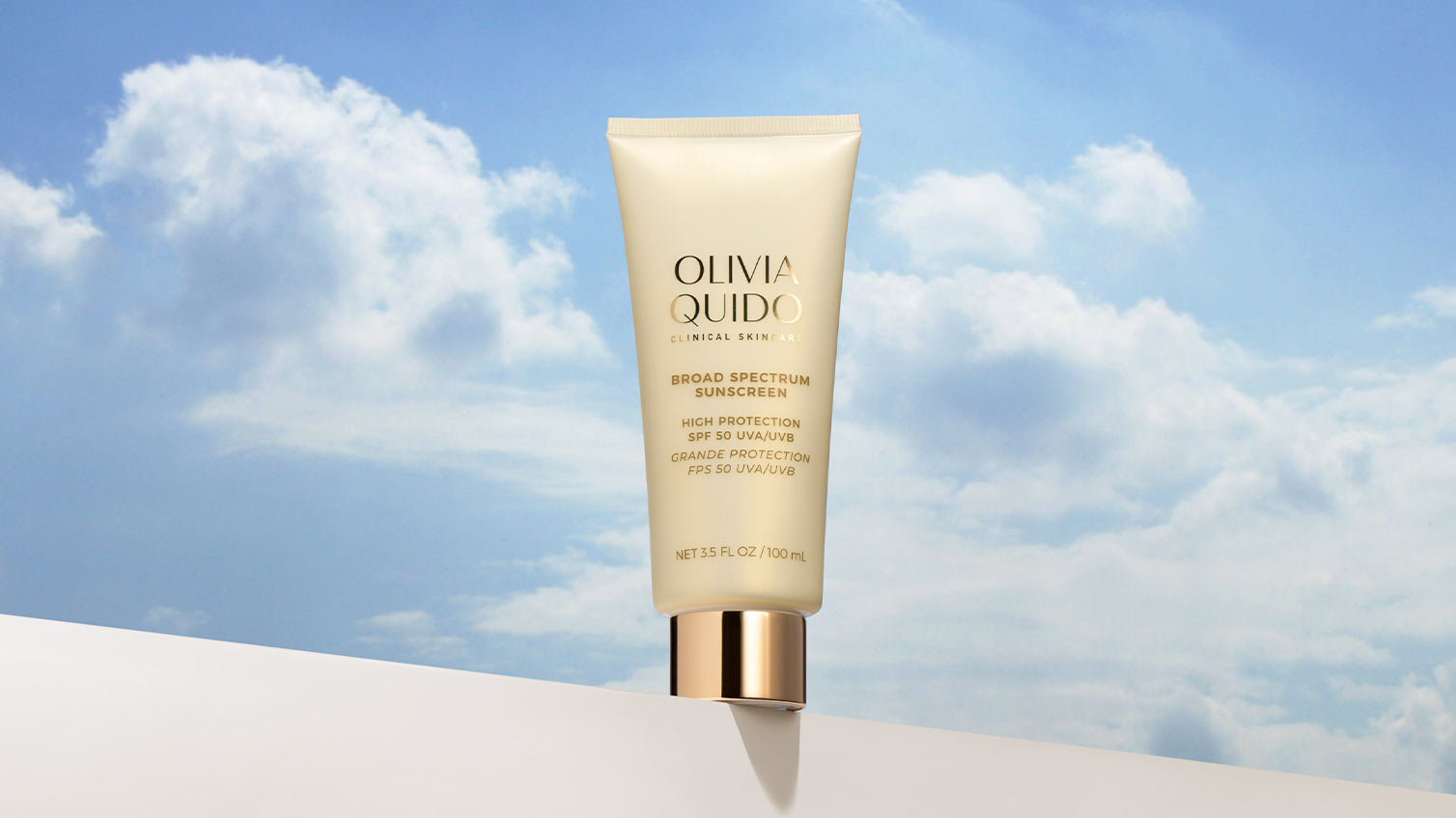 Tube of Olivia Quido Clinical Skincare Broad Spectrum Sunscreen SPF50 sitting on a wall with blue sky and clouds behind